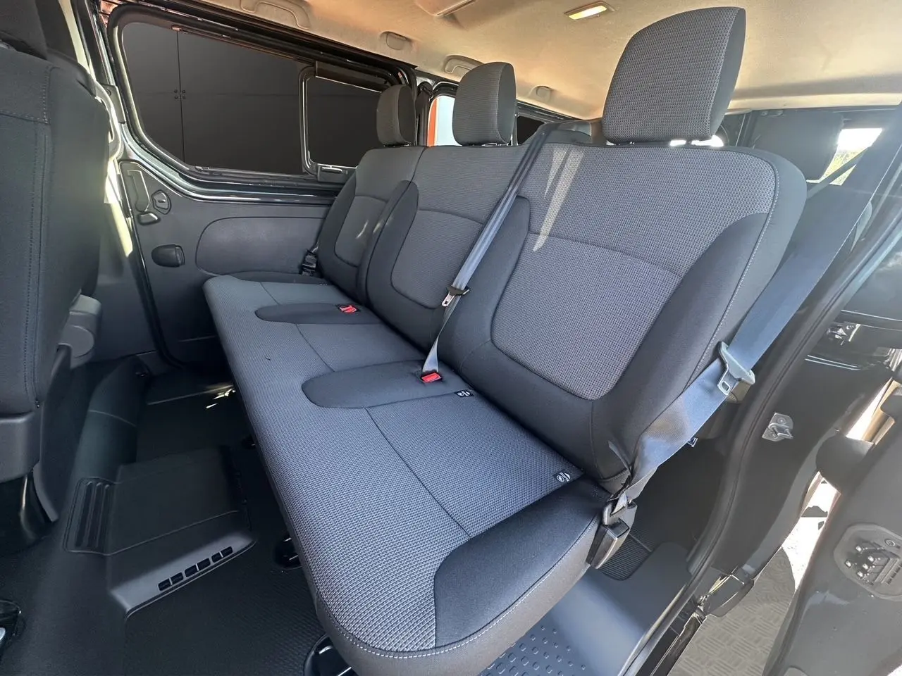 Banquette arrière en tissu noir vue côté droit dans un Renault Trafic Combi gris Comète 2025 avec porte coulissante ouverte.
