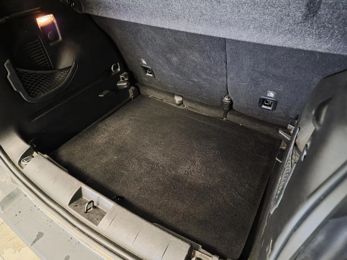 Coffre ouvert du Jeep Renegade blanc, vue plongeante montrant tapis de coffre noir et crochets d'arrimage.