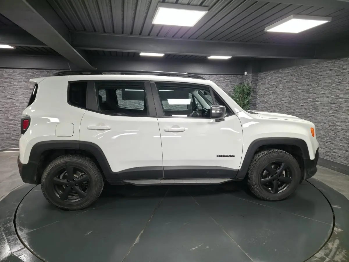 Jeep Renegade blanc vue de profil côté gauche avec jantes noires 5 branches dans un showroom.