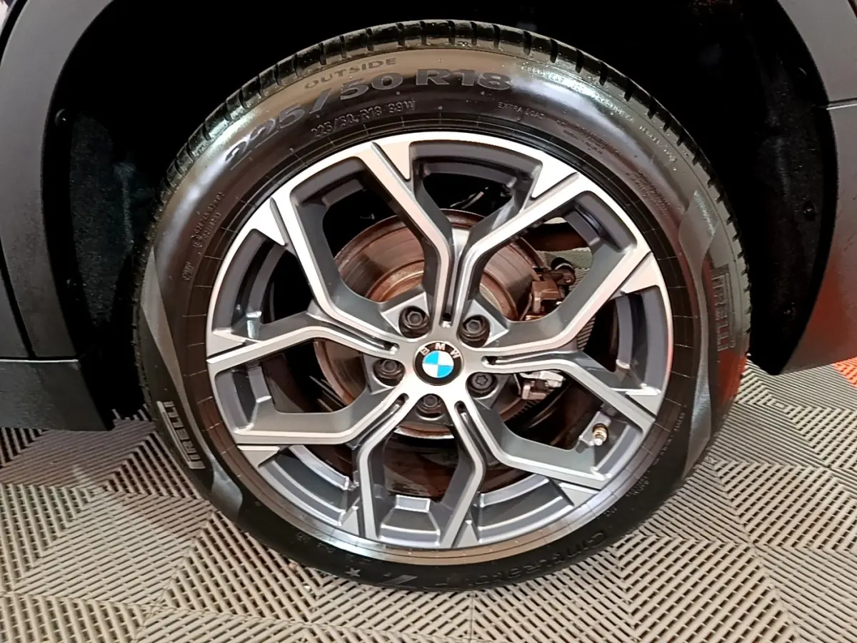 Gros plan sur la roue avant droite d’un BMW X2 noir 2023, jante alliage à design géométrique et pneu Pirelli.