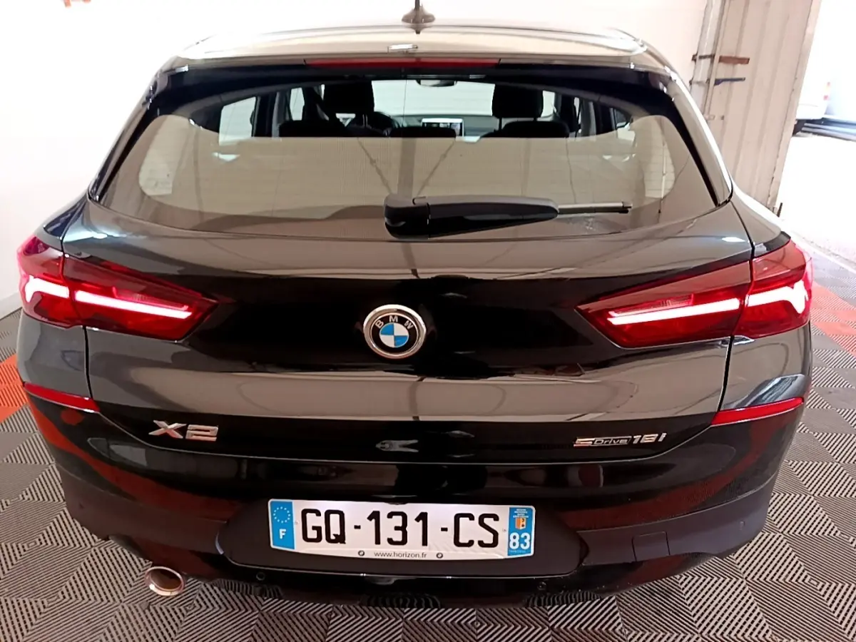 Vue arrière d'une BMW X2 sDrive18i Lounge noire avec feux LED allumés et plaque d'immatriculation française visible.