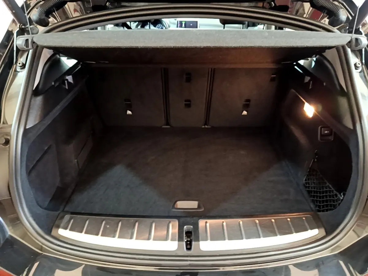 Coffre ouvert noir de BMW X2 sDrive18i Lounge 2023, vue arrière avec éclairage intérieur et filet de rangement.