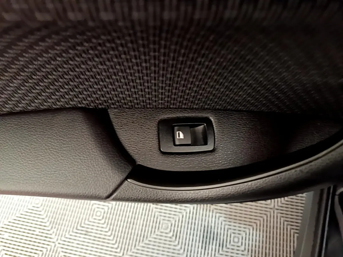 Gros plan sur le bouton de verrouillage de porte noir à l'intérieur de la portière côté conducteur d'une BMW X2 noire.