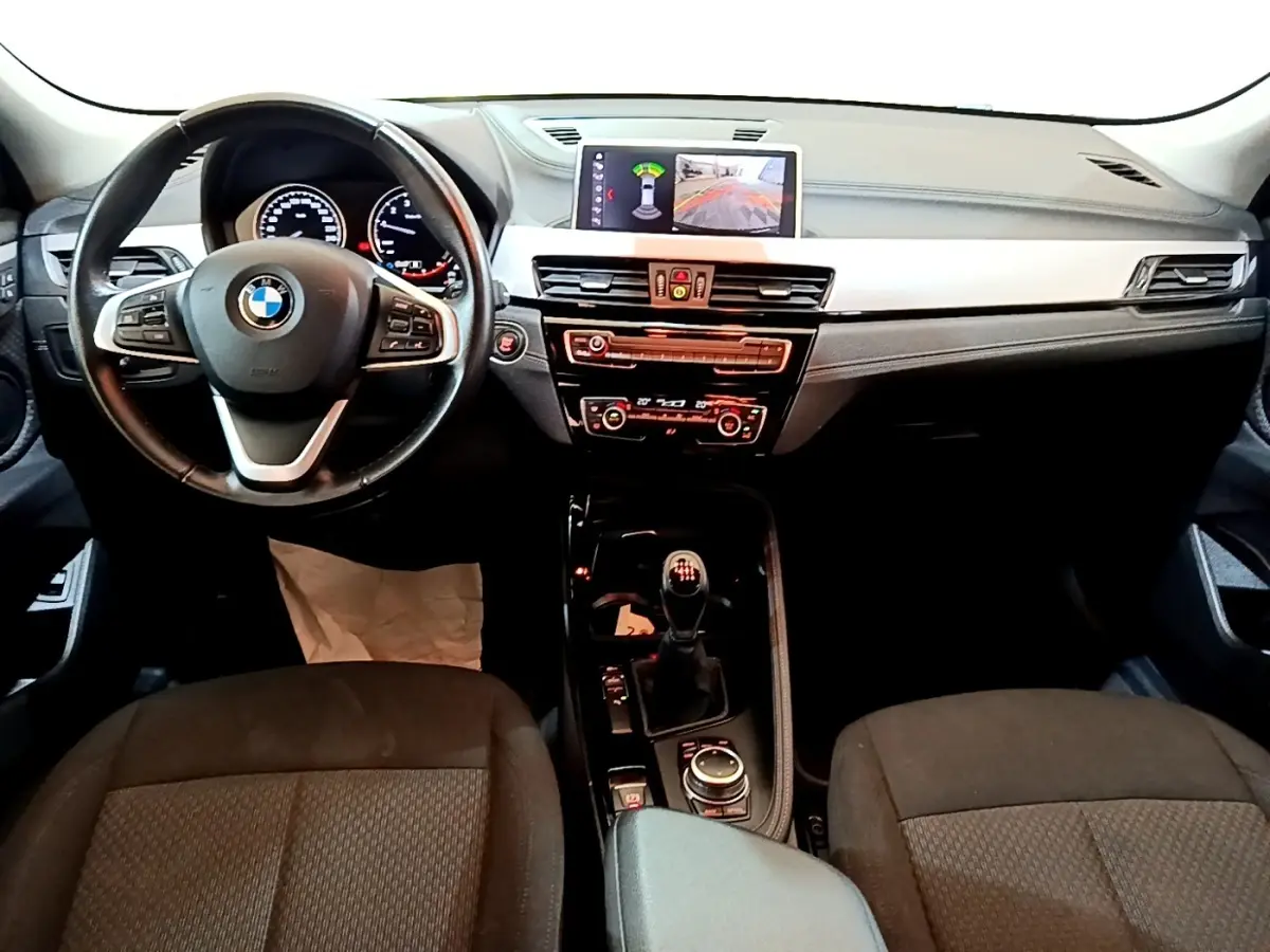 Vue intérieure avant du BMW X2 sDrive18i Lounge 2023 noir, volant cuir, écran central avec affichage caméra de recul.