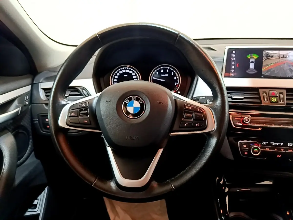 Vue intérieure centrée sur le volant cuir BMW avec tableau de bord et écran d'aide au stationnement affiché.