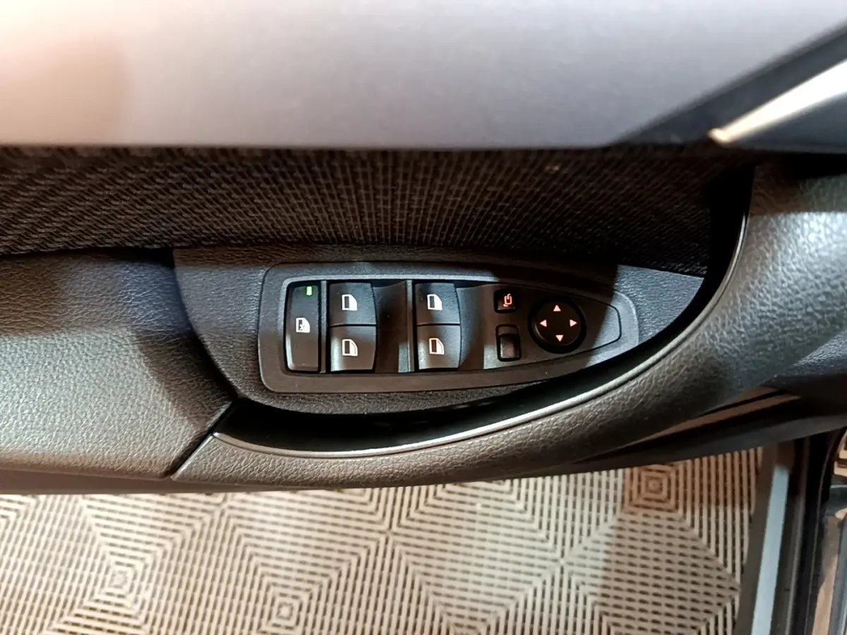 Vue rapprochée des commandes de lève-vitres et rétroviseurs sur la porte côté conducteur d'une BMW X2 noire.