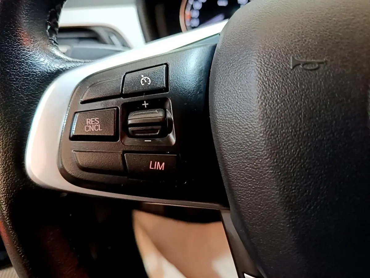 Gros plan sur les commandes du régulateur de vitesse au volant cuir noir d’une BMW X2 sDrive18i Lounge 2023.