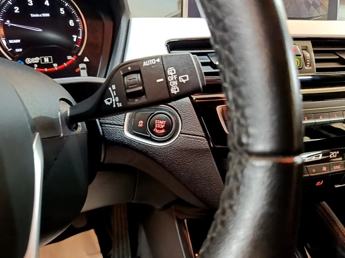 Gros plan sur le volant et le bouton start/stop rouge du tableau de bord noir du BMW X2 sDrive18i Lounge 2023.