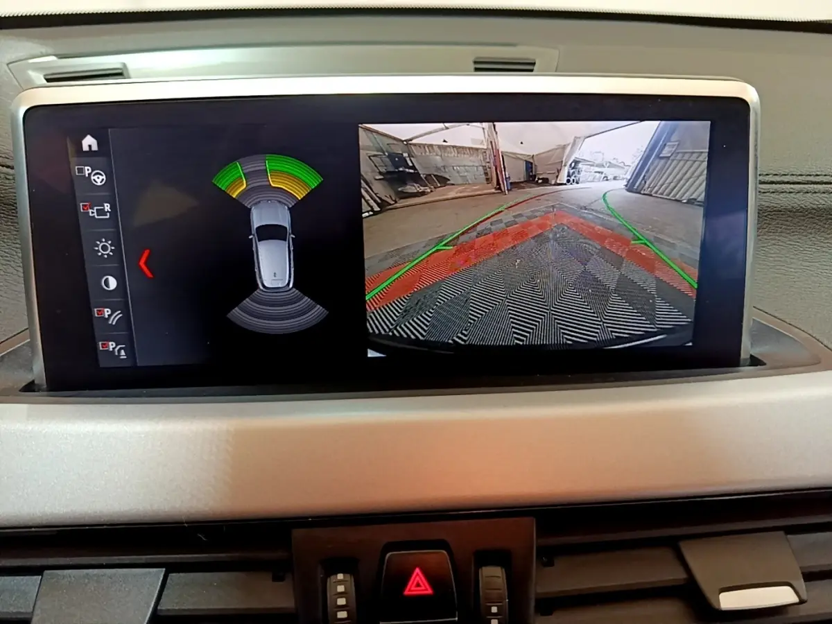 Écran central du BMW X2 sDrive18i 2023 montrant l'aide au stationnement arrière avec caméra et capteurs actifs.