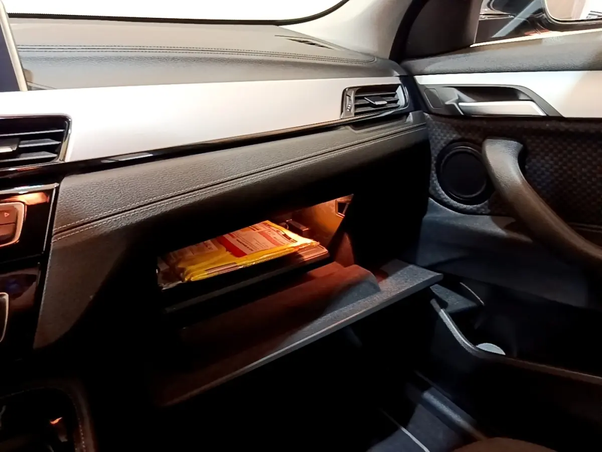 Intérieur BMW X2 sDrive18i 2023 vu côté passager, boîte à gants ouverte avec éclairage intérieur orange.