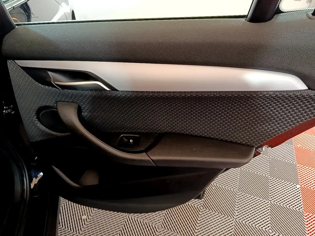Vue intérieure de la porte arrière gauche noire du BMW X2 sDrive18i Lounge avec habillage tissu et commande de lève-vitre.