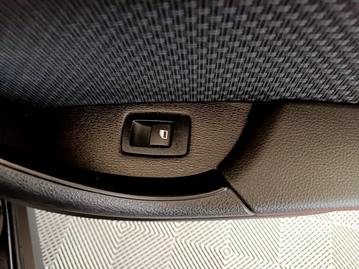 Bouton de commande de lève-vitre arrière droit sur la porte intérieure noire d’un BMW X2 sDrive18i Lounge 2023.