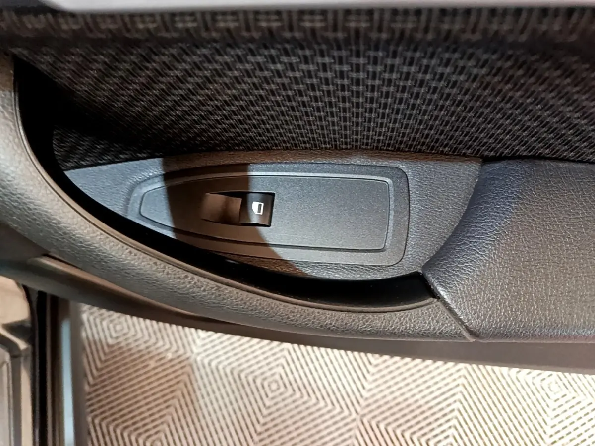 Gros plan sur le bouton de commande de lève-vitre côté gauche intérieur d'une BMW X2 sDrive18i Lounge noire 2023.