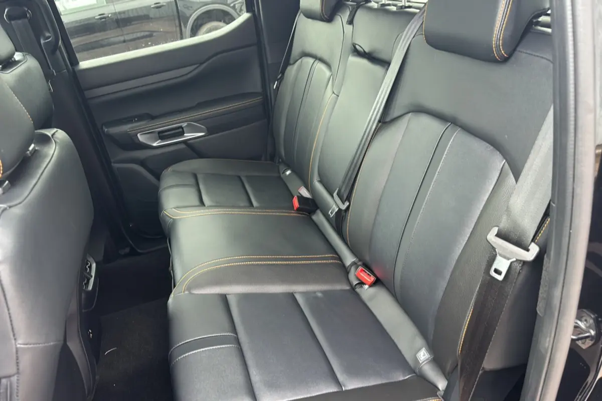 Vue intérieure côté arrière droit du Ford Ranger 3.0 V6 Wildtrak Plus, sièges cuir noirs avec surpiqûres orange.