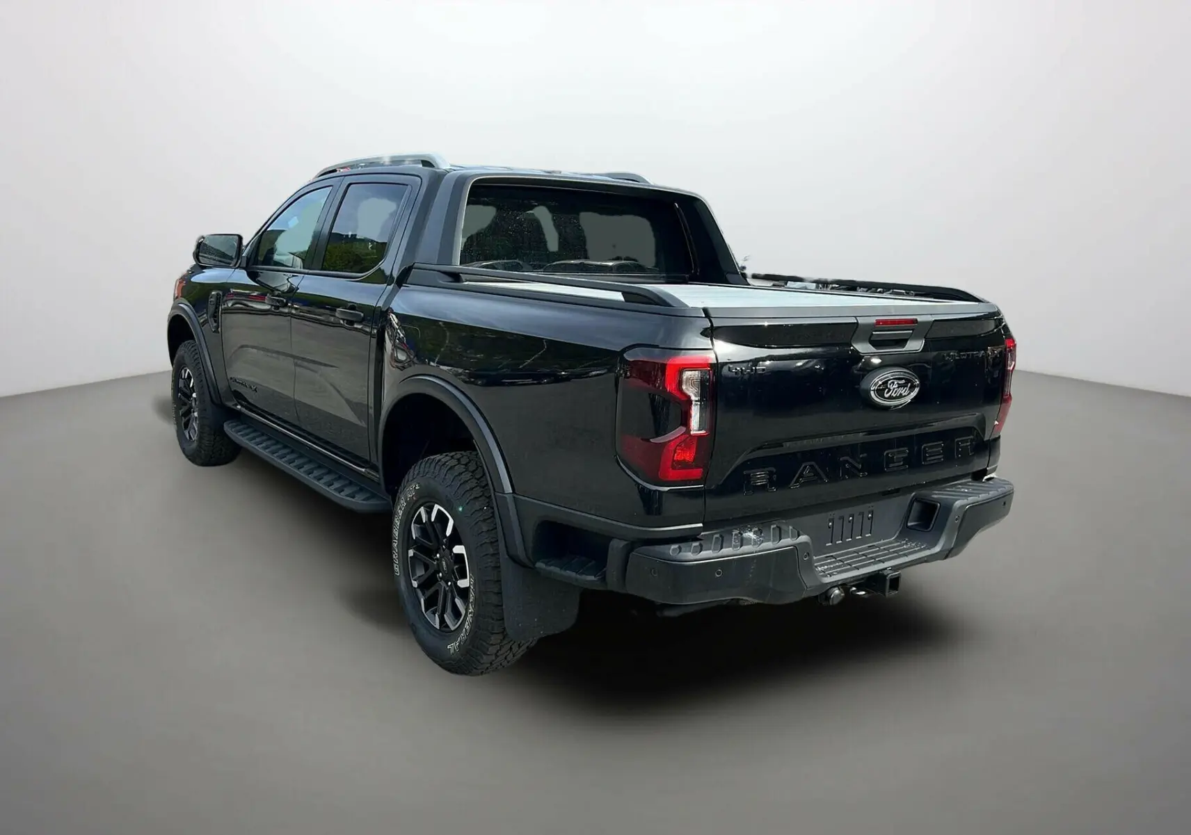 Ford Ranger 205 Wildtrak noir agate vu en 3/4 arrière droit avec barres de toit et ridelle coulissante.