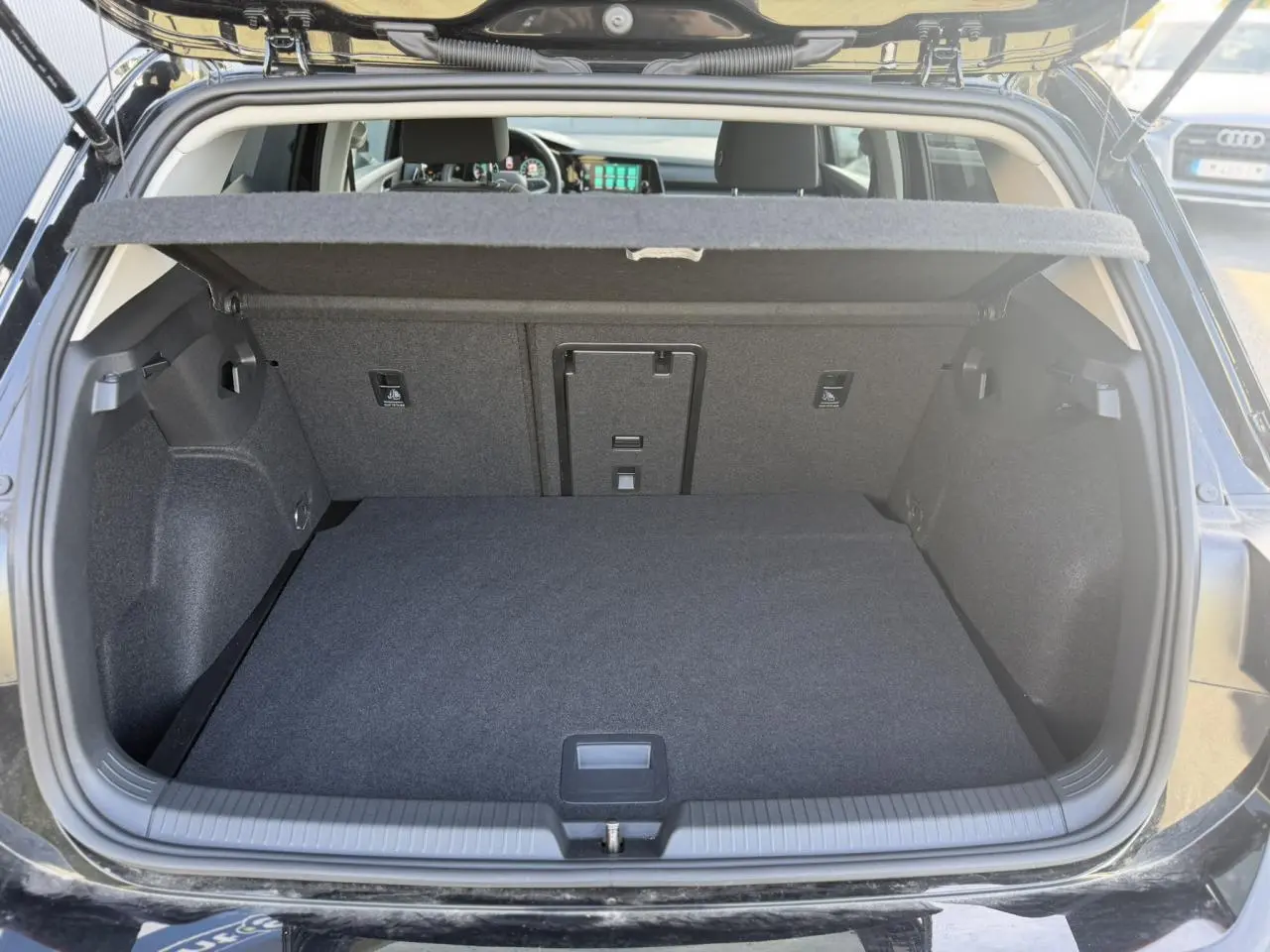 Coffre ouvert d'une Volkswagen Golf VIII noire, vue arrière montrant l'espace de chargement et la plage arrière.