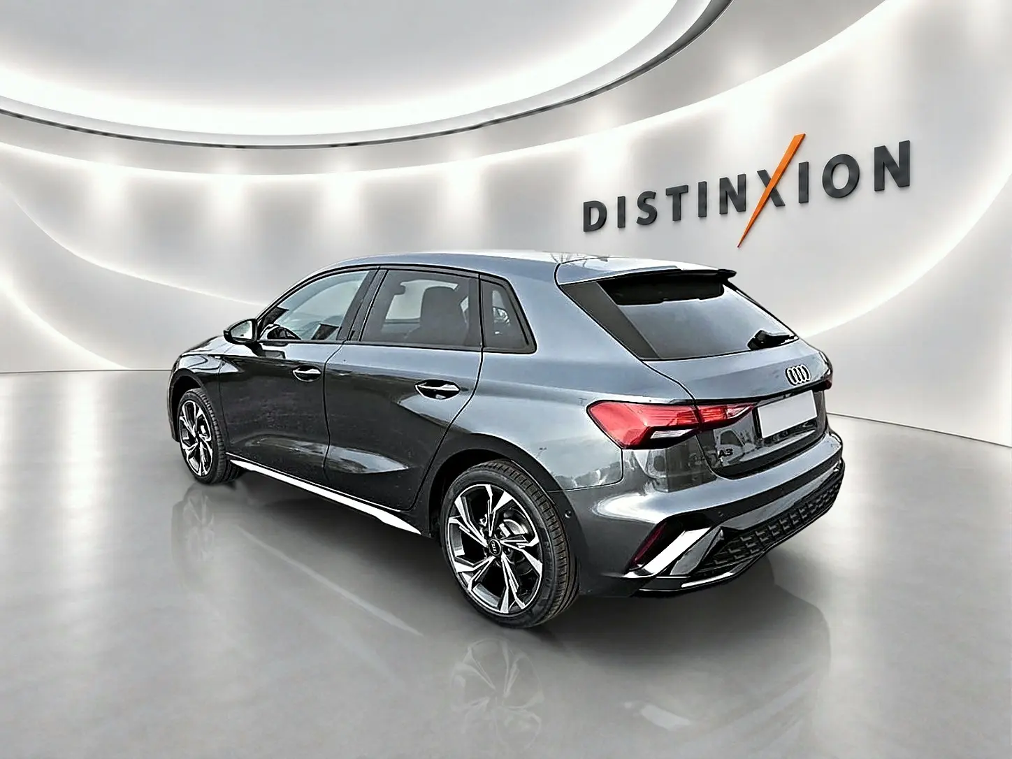 Audi A3 Sportback gris Daytona vue 3/4 arrière droit dans un showroom lumineux avec jantes alu noires.