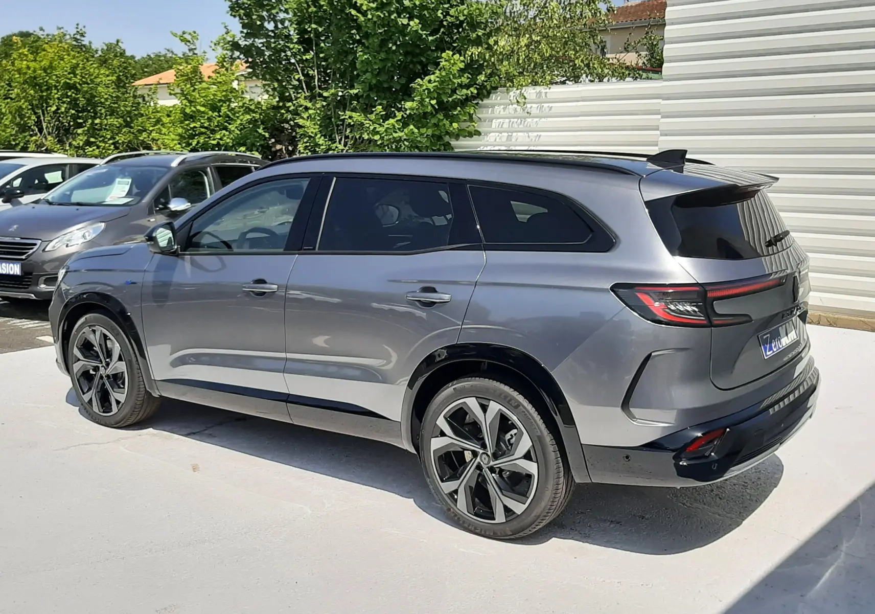 Vue 3/4 arrière droite d'un Renault Espace VI gris schiste métallisé avec jantes noires et toit noir dans un parking extérieur.