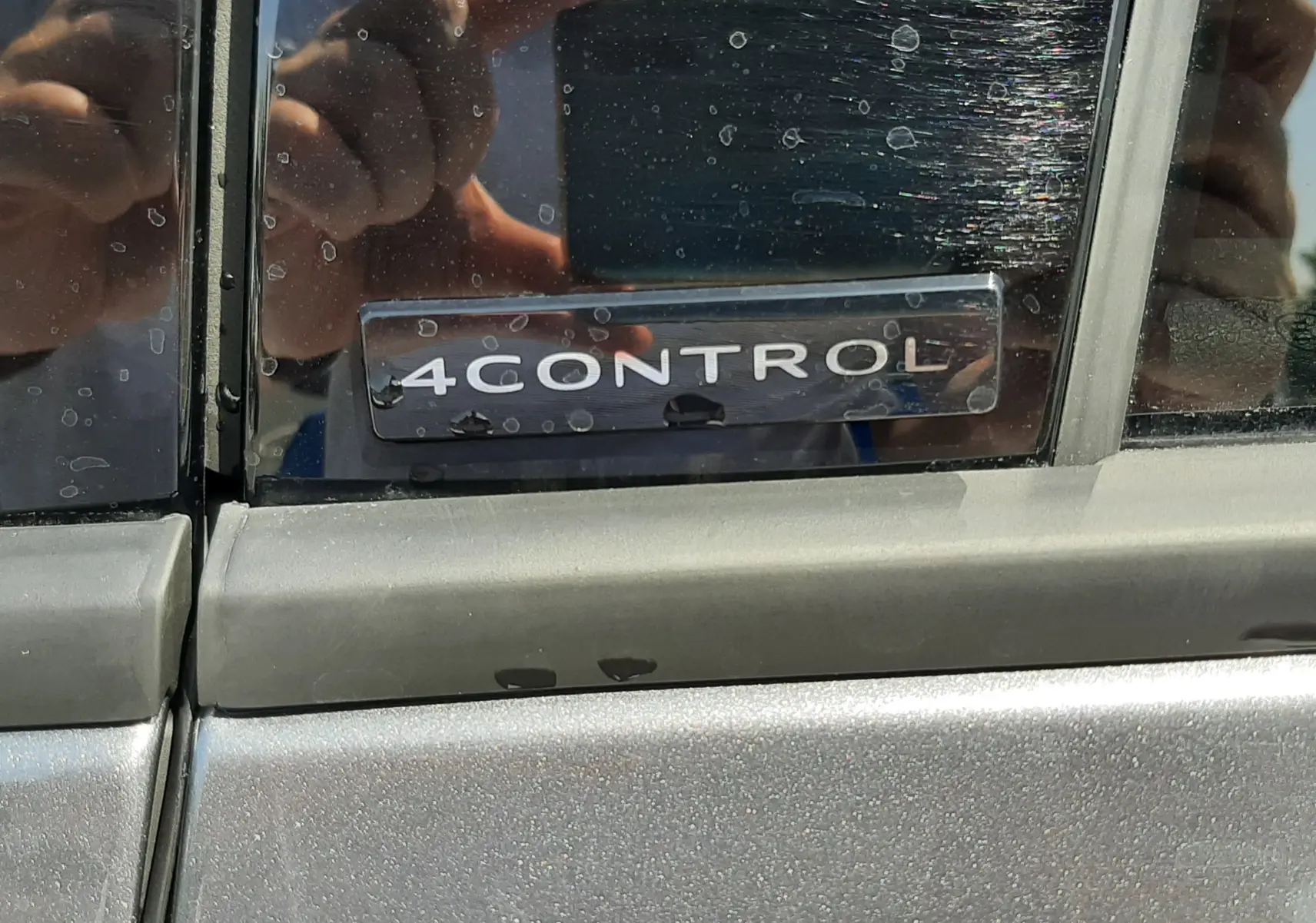 Gros plan sur l'écusson 4CONTROL sur la porte d'une Renault Espace gris schiste métal, reflet de la personne prenant la photo.