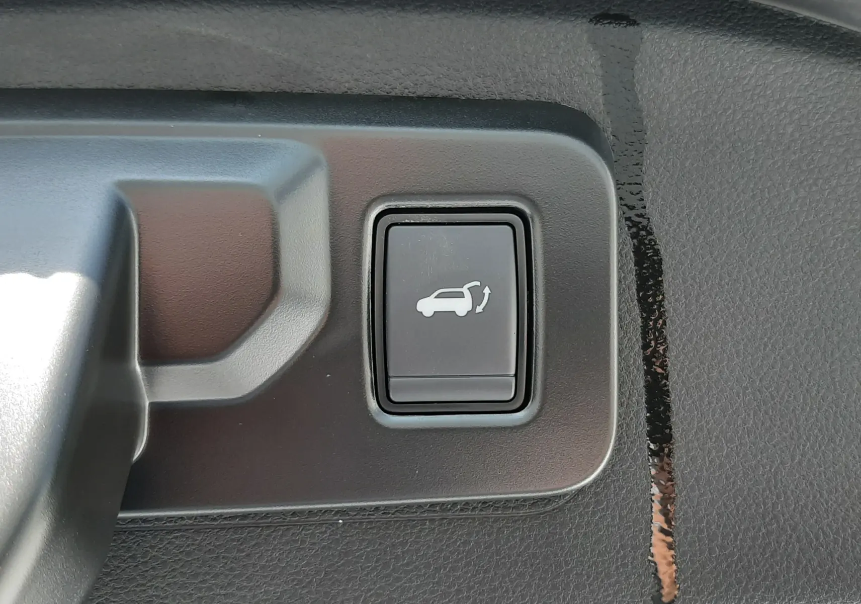 Bouton noir de commande d'ouverture du coffre sur la garniture intérieure d'un Renault Espace VI gris schiste métal.