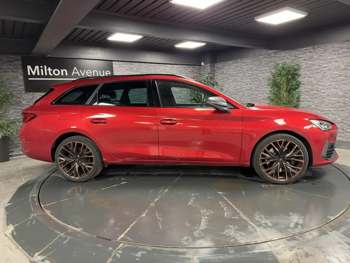 Profil droit d'une CUPRA Leon Sportstourer rouge Désir avec jantes alliage 19 pouces Palm Springs en intérieur showroom.