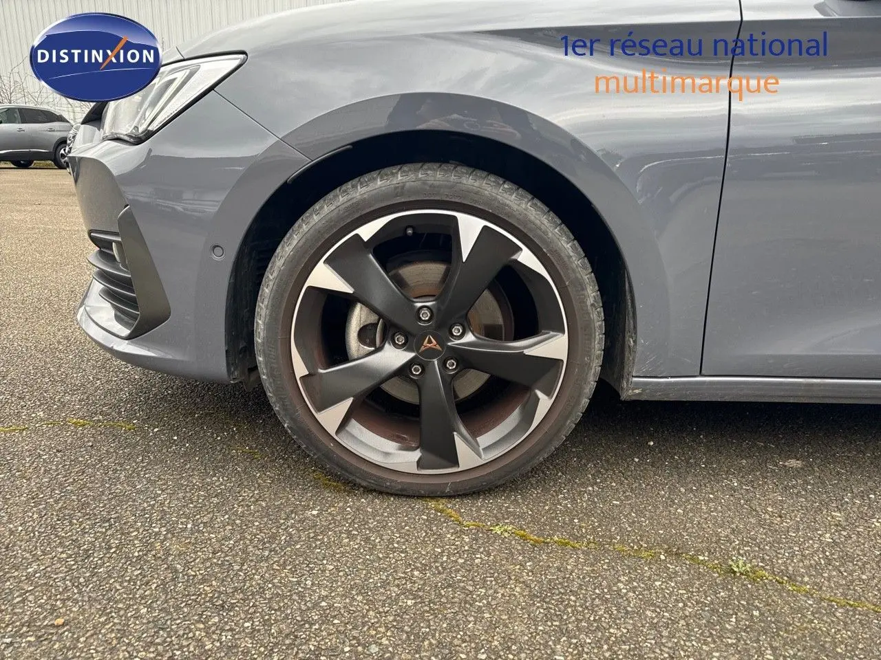 Gros plan sur la roue avant gauche et l'aile d'une CUPRA LEON ST gris Graphene metal avec jante bi-ton distinctive.