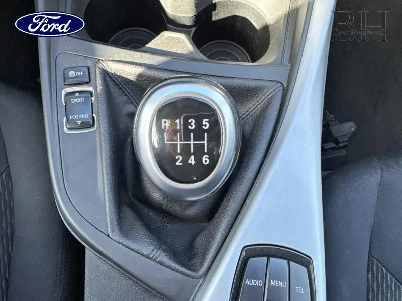 Gros plan sur le levier de vitesses manuel entouré de commandes, intérieur tissu noir de la BMW Série 1 114i Lounge.