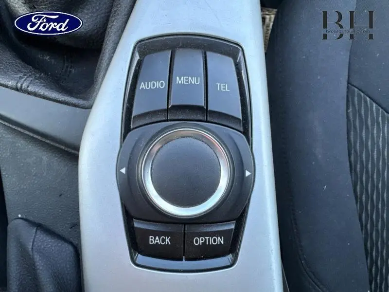 Gros plan sur la molette de commande multimédia noire et argentée dans l'habitacle d'une BMW Série 1 114i noire.