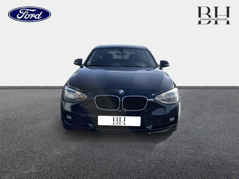 BMW Série 1 114i noire vue de face, mettant en valeur sa calandre double haricot et ses phares halogènes.
