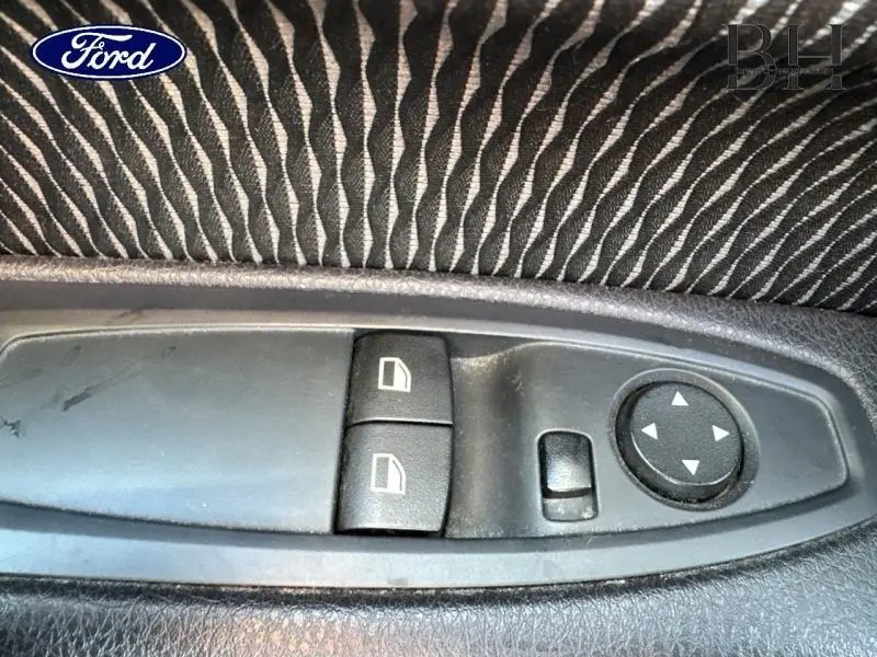 Panneau de commandes des vitres et rétroviseurs côté conducteur avec tissu noir à motifs ondulés.