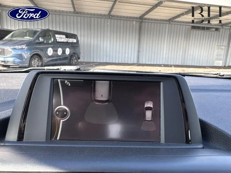 Vue intérieure du tableau de bord de la BMW Série 1 114i 2013, écran multifonction affichant l'aide au stationnement.