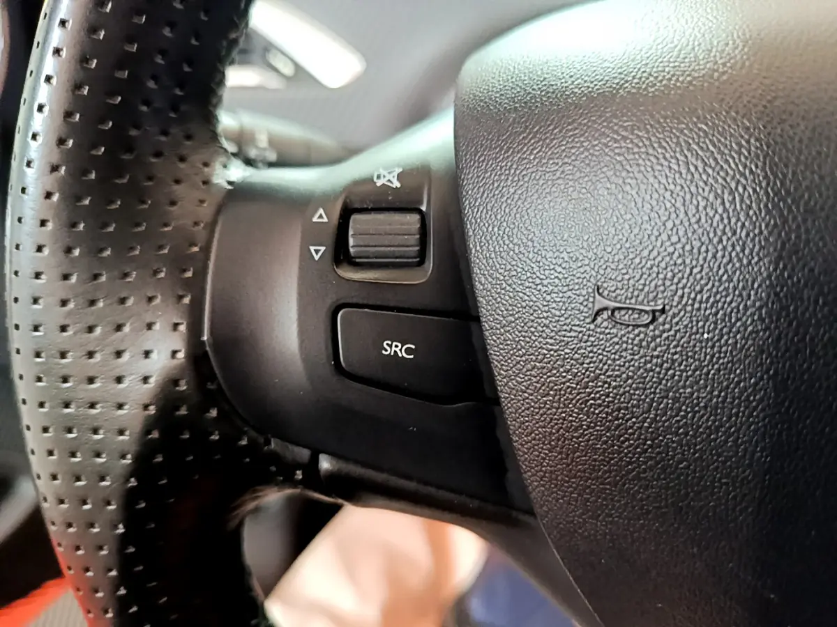 Gros plan sur la partie gauche du volant cuir perforé du Peugeot 2008 gris foncé, avec commandes audio intégrées.