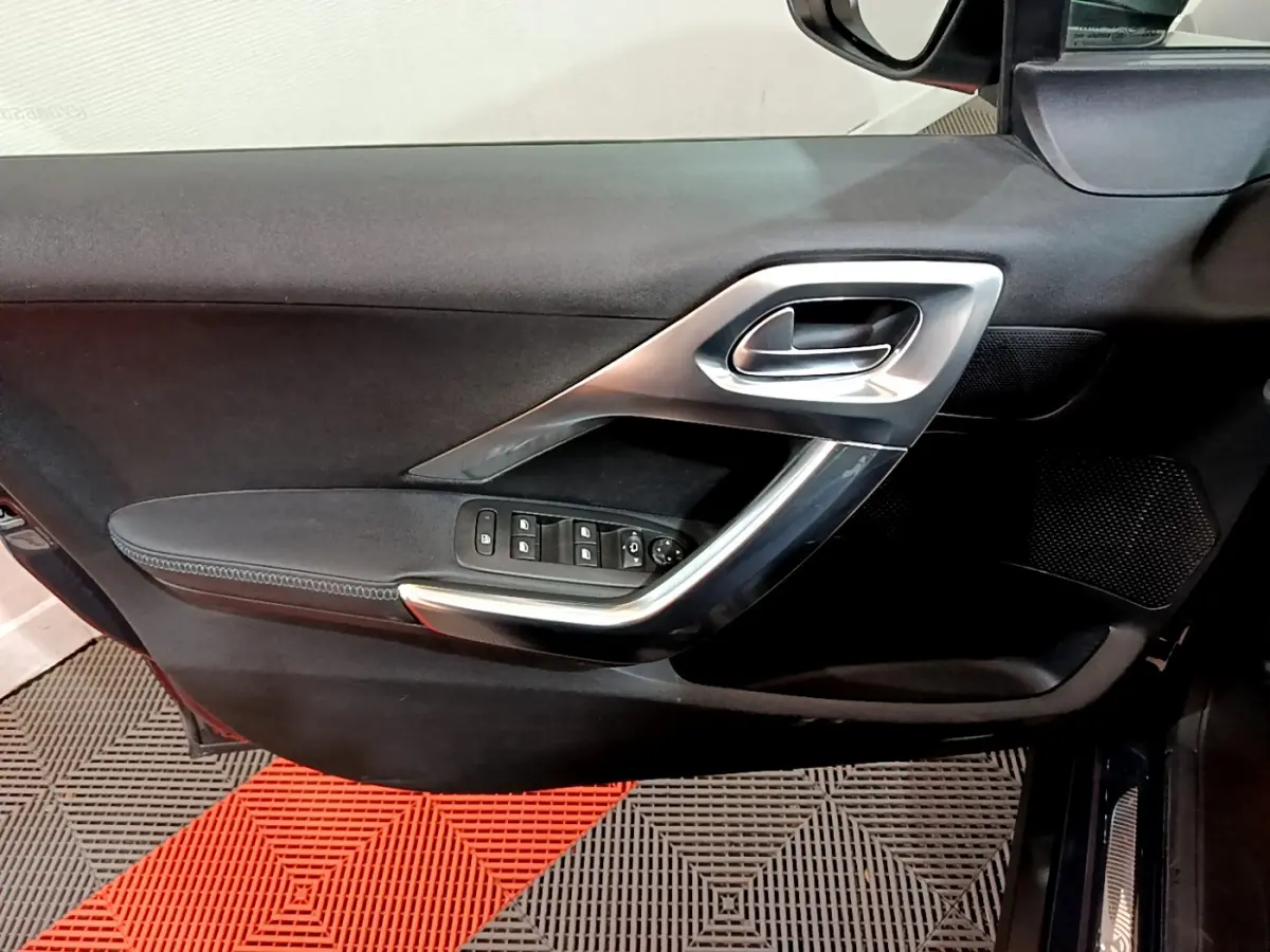 Vue intérieure côté gauche de la porte avant d'une Peugeot 2008 gris foncé avec commandes de vitres et poignée argentée.