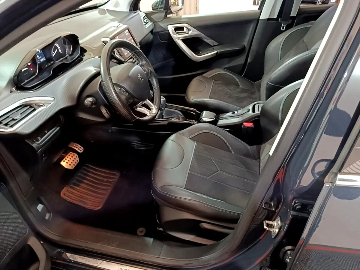 Intérieur vue côté conducteur du Peugeot 2008 gris foncé, volant cuir et sièges noirs avec surpiqûres bleues.