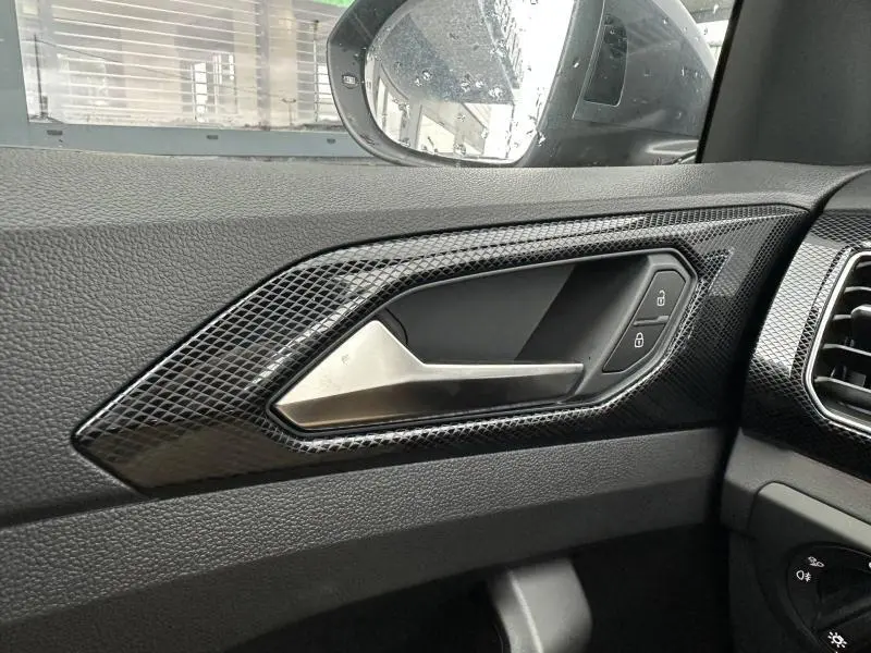 Poignée de porte intérieure côté gauche du Volkswagen T-Cross 2025 en finition R-Line avec insert noir brillant et boutons de verrouillage.