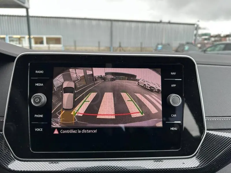 Écran central du Volkswagen T-Cross 2025 montrant la caméra de recul avec vue arrière sur un passage piéton et voitures garées.