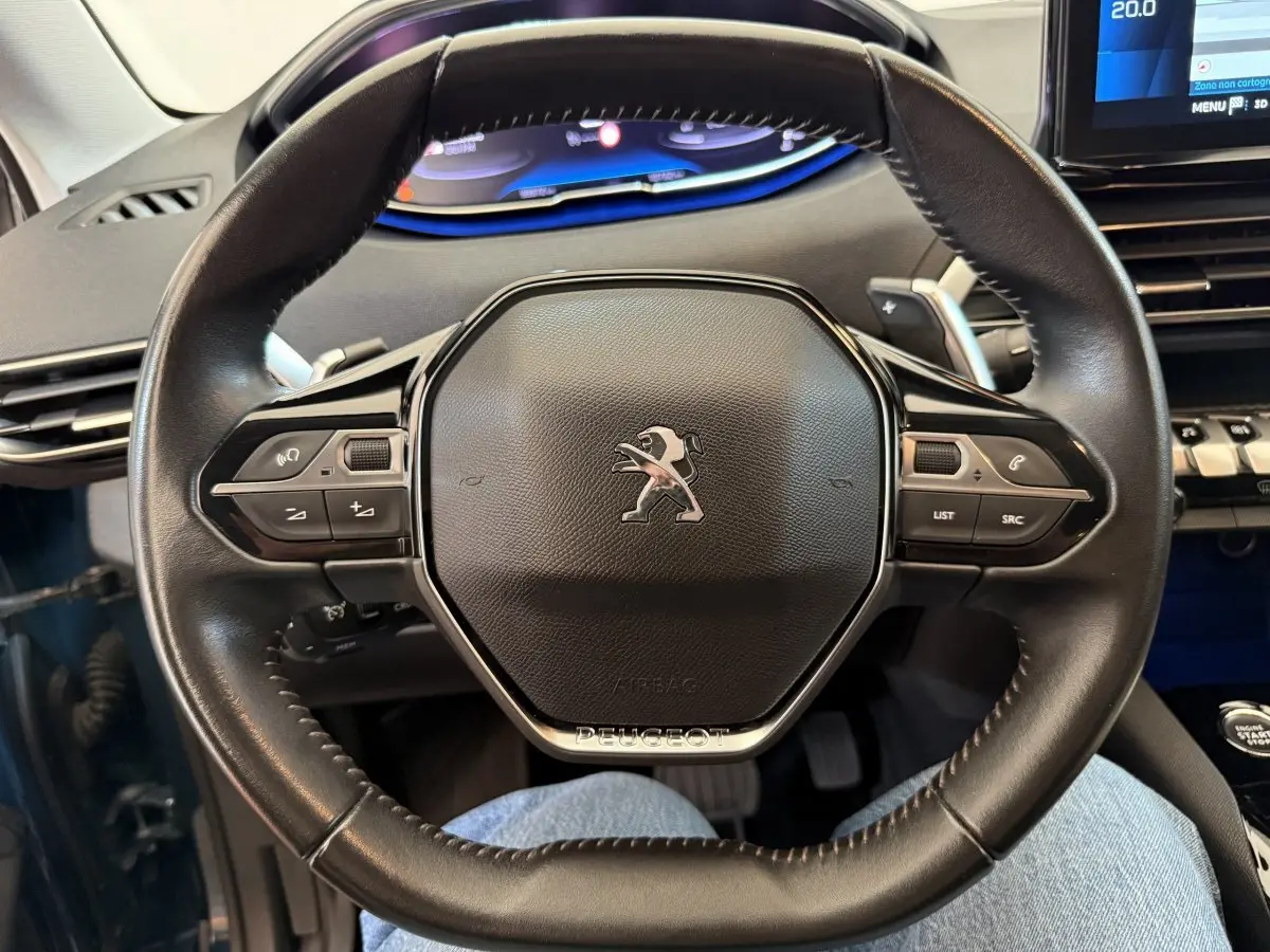 Vue rapprochée du volant cuir noir du Peugeot 3008 2021 avec tableau de bord numérique et écran tactile visible en arrière-plan.