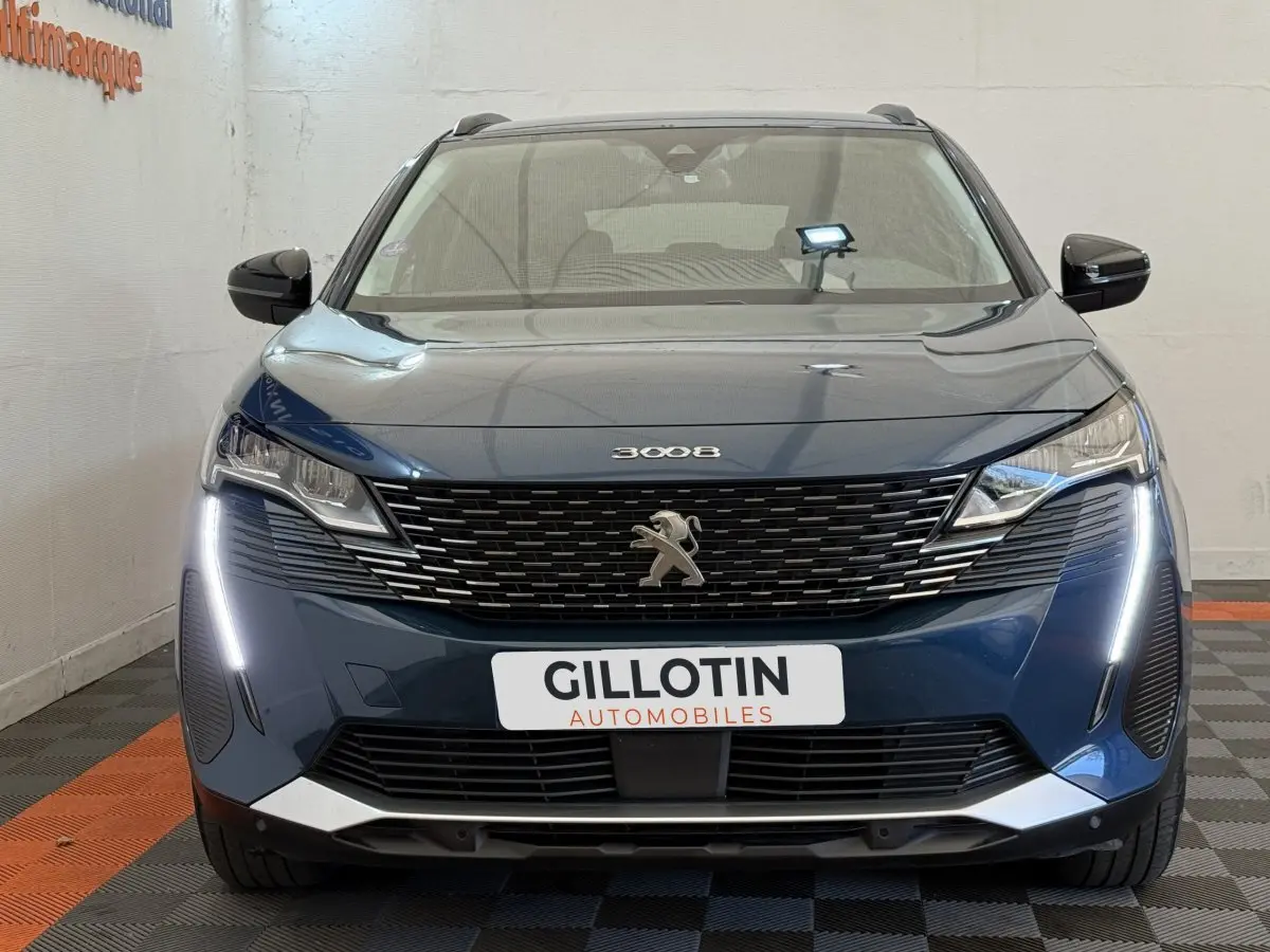 Vue frontale d'un Peugeot 3008 bleu avec calandre noire et feux LED en forme de griffes allumés.