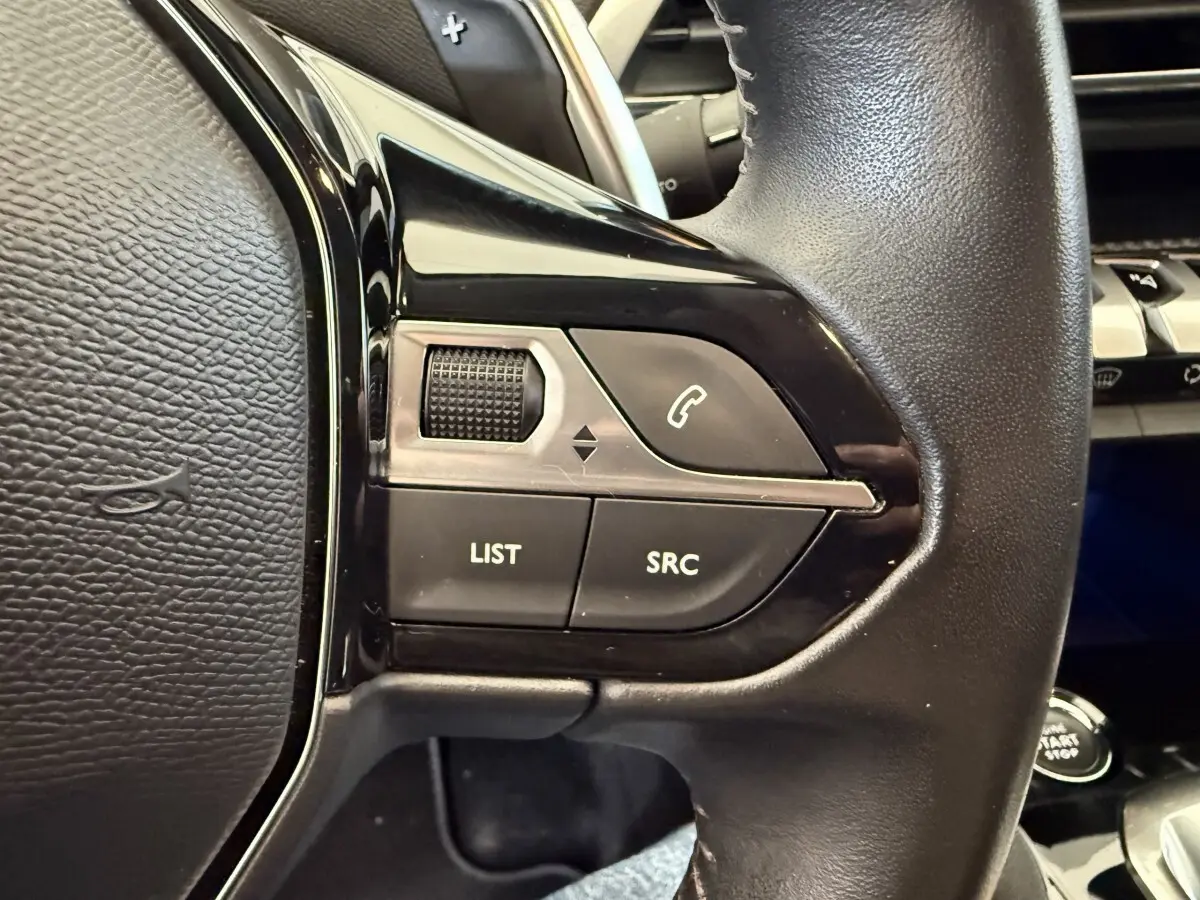 Gros plan sur les commandes gauche du volant cuir noir du Peugeot 3008 bleu, avec boutons LIST, SRC et téléphone.