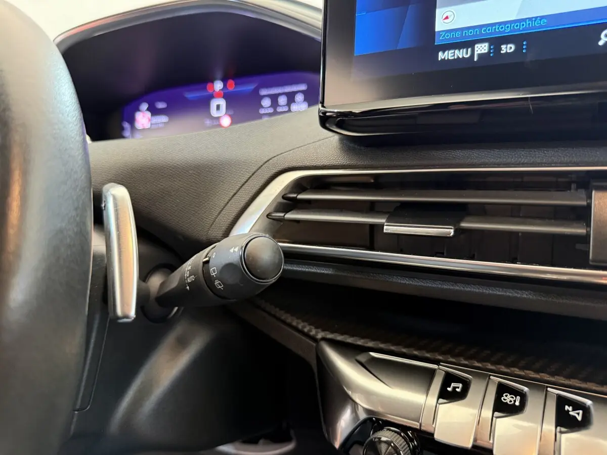 Gros plan sur le tableau de bord noir du Peugeot 3008 bleu, avec écran tactile et commandes de climatisation visibles.