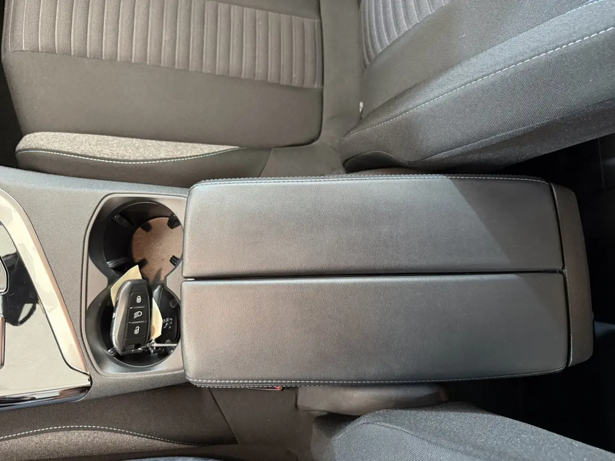 Vue rapprochée de l'accoudoir central noir et porte-gobelets avec clé de Peugeot 3008 bleu, intérieur tissu gris.