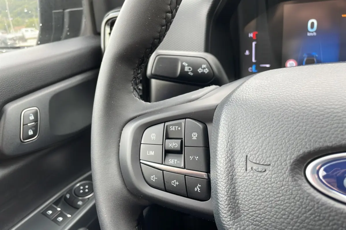 Gros plan sur le volant cuir du Ford Ranger gris carbone, avec commandes multifonctions et tableau de bord numérique visible.