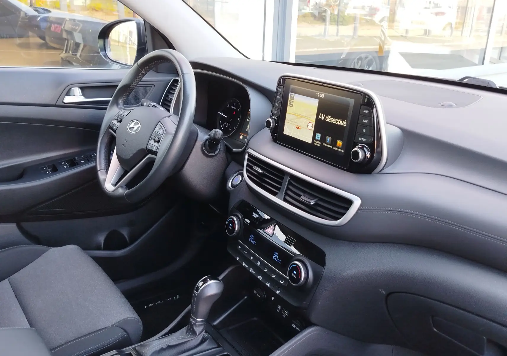 Vue intérieure côté conducteur du Hyundai Tucson 2019, tableau de bord gris avec écran tactile et volant cuir multifonction.
