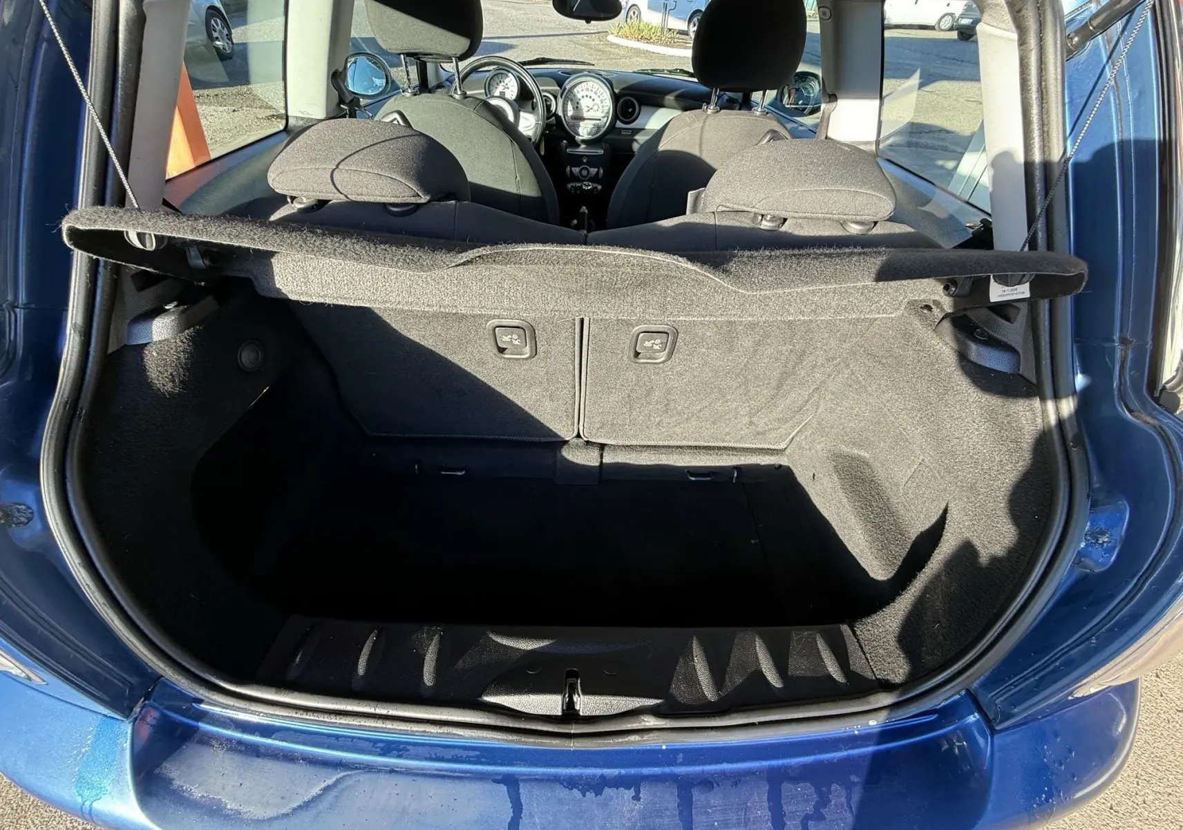 Coffre ouvert vu de l'arrière d'une MINI Cooper bleu, montrant l'intérieur noir et les sièges avant.