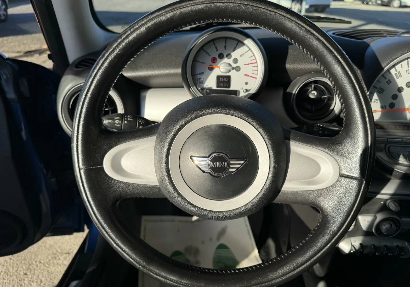 Vue intérieure centrée sur le volant en cuir noir de la MINI Cooper bleu 2007 avec tableau de bord clair en arrière-plan.