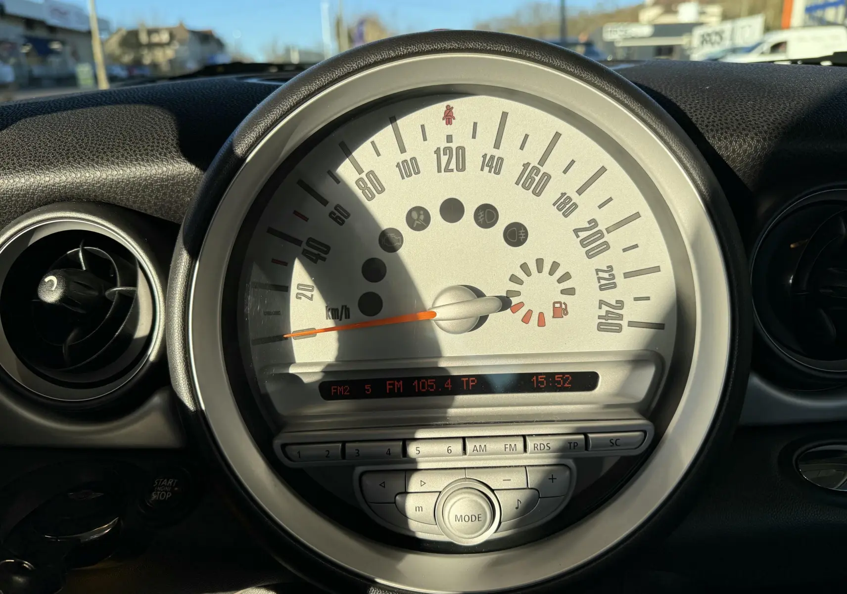 Vue rapprochée du compteur central blanc d'une MINI Cooper 2007 avec affichage radio et heure à 15h52.