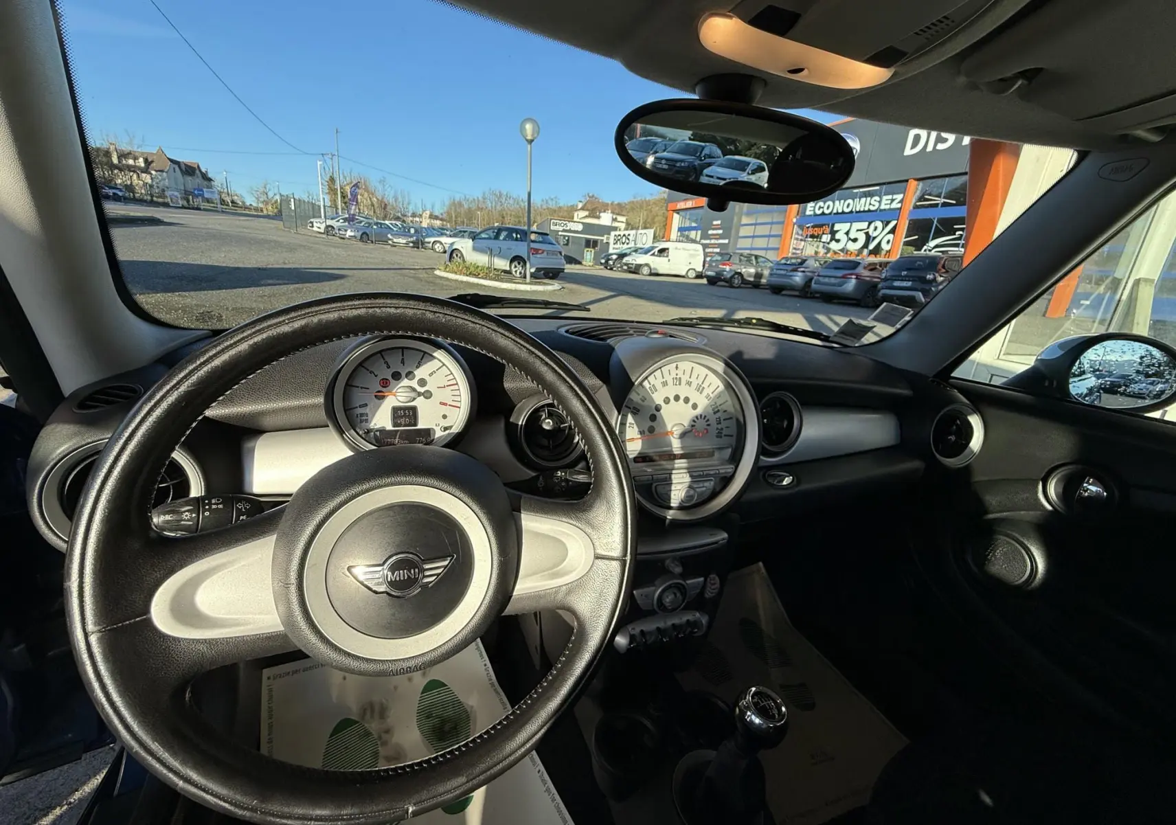 Vue intérieure du tableau de bord et volant cuir noir d'une MINI Cooper 2007 avec compteur central blanc.