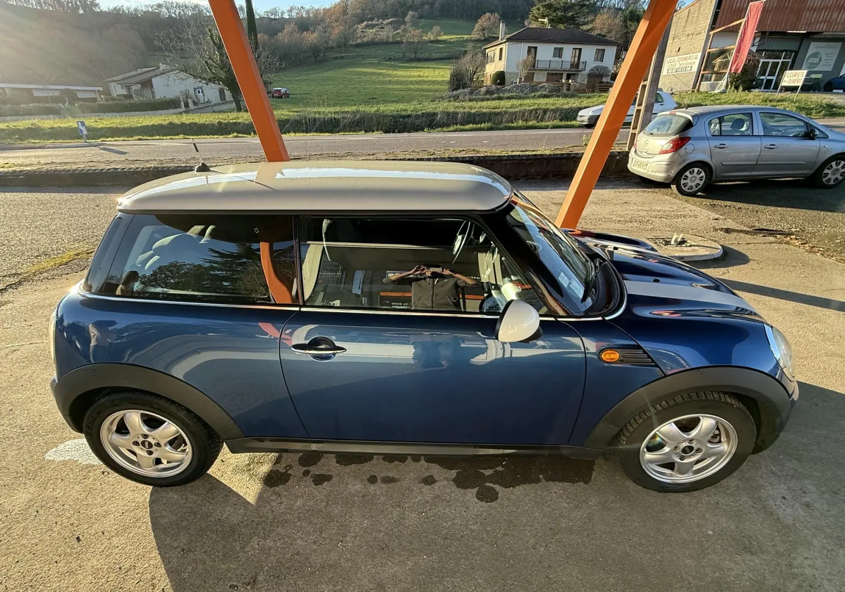 Vue latérale droite d'une MINI Cooper 1.6 bleu avec toit blanc sous un abri en extérieur.