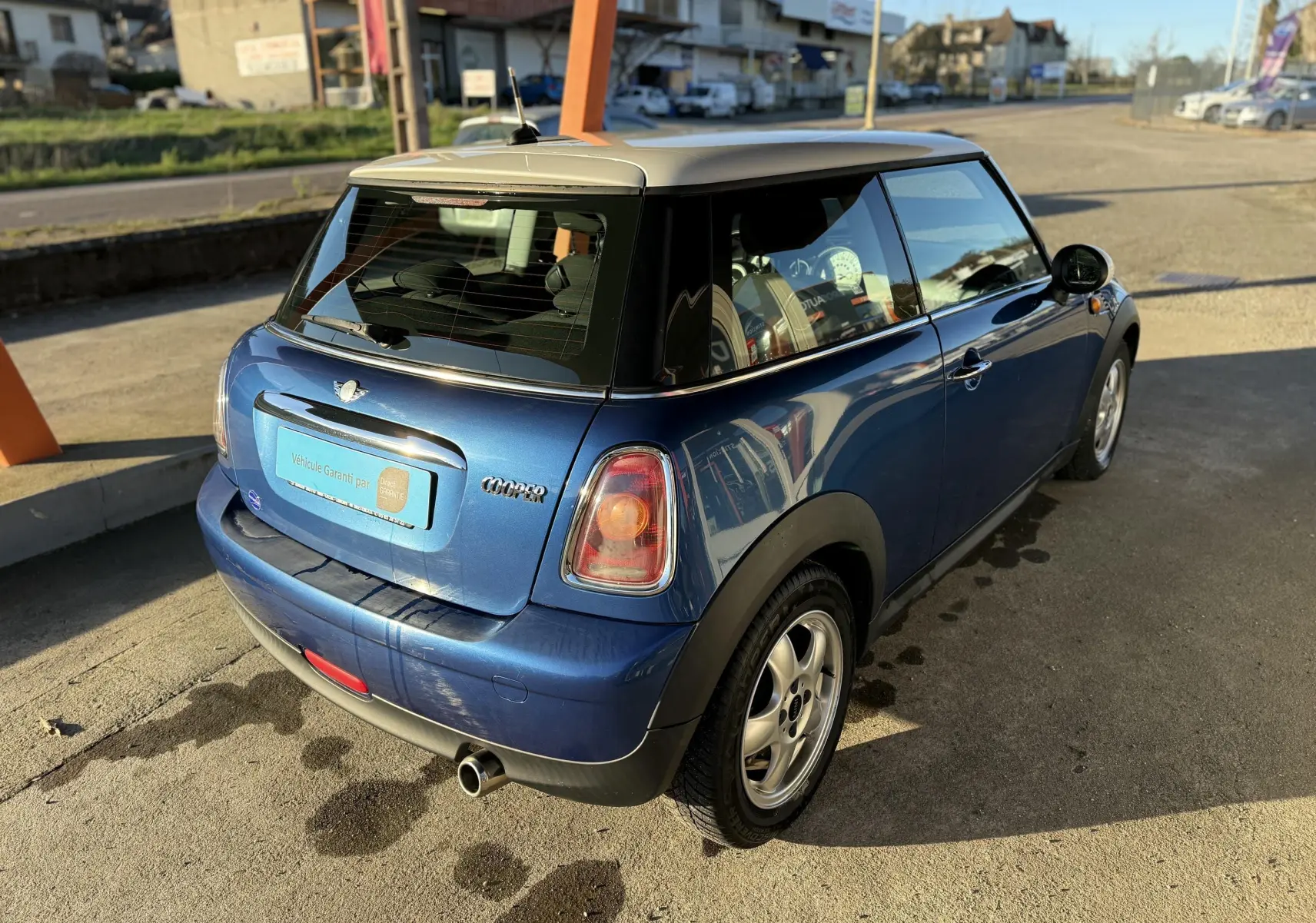 Vue 3/4 arrière droite d'une MINI Cooper 2007 bleu avec toit blanc et jantes alliage 15 pouces.