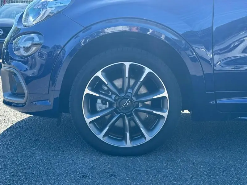 Gros plan sur la roue avant gauche d'une FIAT 500X rouge avec jante alu au design distinctif en étoile.